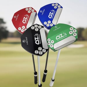 Puede incluir: Cuatro putters de golf en rojo, negro, azul y verde. Cada putter tiene una cara plateada y el texto "OZli" y "LAB GOLF". Los putters tienen varillas plateadas y negras, sobre un fondo borroso de campo de golf verde.