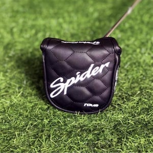 Puede incluir: Funda negra para la cabeza del palo de golf con la inscripci&oacute;n blanca "Spider" y costuras de diamante. La funda est&aacute; sobre una superficie verde y el palo de golf es parcialmente visible. La palabra "TOUR" est&aacute; impresa en blanco en la parte inferior de la funda.