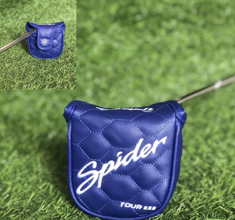 Puede incluir: Una funda de putter de golf azul acolchada con la palabra "Spider" en escritura blanca. La funda est&aacute; sobre una superficie de hierba verde. El putter est&aacute; parcialmente insertado en la funda.