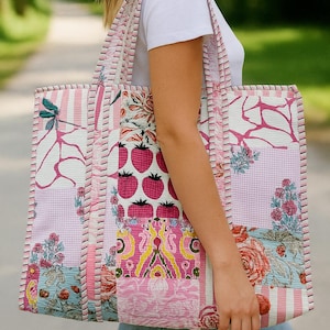 Peut inclure: Un grand sac fourre-tout patchwork avec une variété de motifs roses et blancs, dont des rayures, du vichy et des motifs floraux. Le sac présente un motif de fraises et est bordé de coutures roses. Le sac fourre-tout a deux poignées.