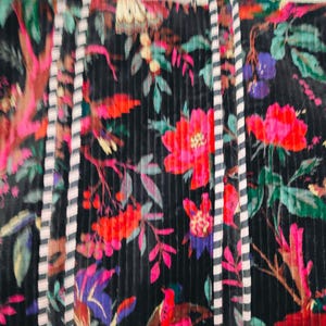 Puede incluir: Un bolso tote negro con un vibrante estampado floral con flores rojas, rosas y moradas, hojas verdes y p&aacute;jaros. El bolso tiene asas y ribetes a rayas.