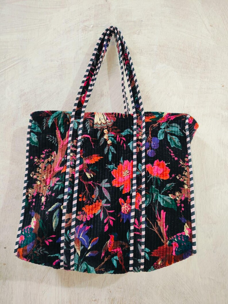 Puede incluir: Bolso tote negro con un vibrante estampado floral en tonos rojos, rosas y morados. El bolso tiene asas y ribetes a rayas. El dise&ntilde;o incluye p&aacute;jaros y follaje.