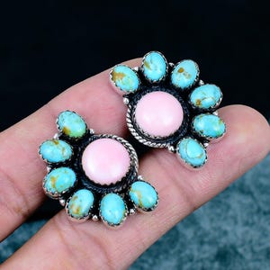 May include: A pair of earrings featuring a central round pink stone surrounded by a cluster of oval turquoise stones with brown matrix, all set in a dark oxidised silver metal frame with a twisted rope detail around the centre stone.