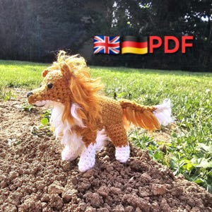 May include: A crocheted dog figurine with brown and white yarn. The dog has a fluffy mane and tail, and is standing on a pile of dirt. The image includes the text "PDF" and flags of the UK and Germany.