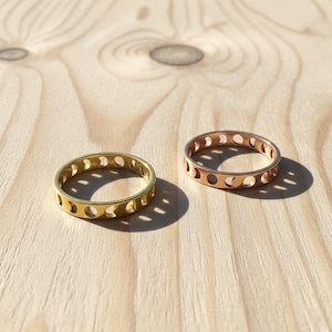 Könnte beinhalten: Zwei Ringe mit einem Himmelsdesign. Ein Ring ist goldfarben, der andere roségoldfarben. Jeder Ring hat eine Reihe von Halbmond-Ausschnitten um das Band. Die Ringe werden auf einer hellen Holzoberfläche präsentiert.
