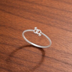 May include: A silver ring with a delicate design featuring two intertwined symbols. The ring is set against a warm, brown wooden surface, highlighting its polished finish. The ring's design is a symbol of the LGBTQ+ community.