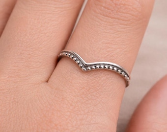 Puede incluir: Un anillo de plata en forma de chevrón con una delicada textura de cuentas a lo largo de la banda exterior. El anillo tiene una punta en forma de V en el centro y un acabado metálico pulido, mostrando un diseño simple y limpio.