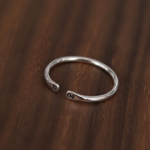 Könnte beinhalten: Ein silberfarbener offener Ring mit einer glatten, polierten Oberfläche. Die beiden Enden des Rings sind leicht abgeflacht und mit den schwarzen Ziffern 11 auf der einen und 04 auf der anderen Seite versehen, was ein schlichtes Design ergibt.