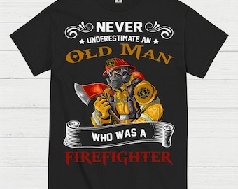 May include: Black t-shirt featuring a graphic of a firefighter in yellow gear, holding an axe. The text reads "NEVER UNDERESTIMATE AN OLD MAN WHO WAS A FIREFIGHTER" in white, gold, and red.