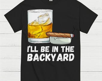 May include: Black t-shirt featuring a graphic of a whiskey glass with ice cubes, a lit cigar, and an ashtray. The text "I'LL BE IN THE BACKYARD" is printed in white below the graphic.