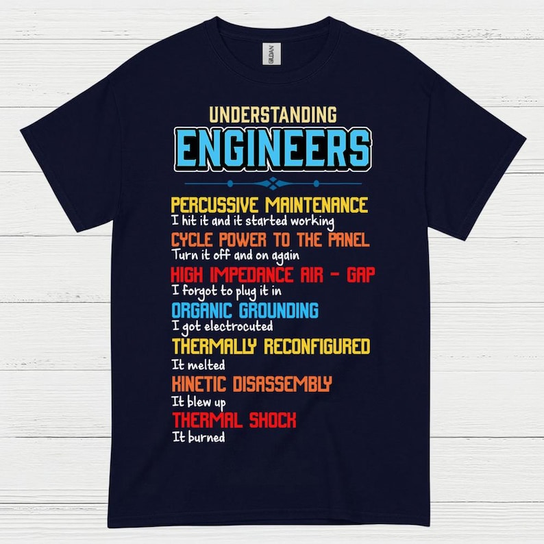 May include: A navy blue t-shirt featuring the text "UNDERSTANDING ENGINEERS" in blue and white. The shirt displays a list of engineering terms in various colours, such as "PERCUSSIVE MAINTENANCE" and "THERMAL SHOCK".