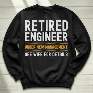 May include: Black sweatshirt with white text that reads "RETIRED ENGINEER UNDER NEW MANAGEMENT SEE WIFE FOR DETAILS". The text is in a bold, sans-serif font. The sweatshirt has a crew neck and long sleeves.