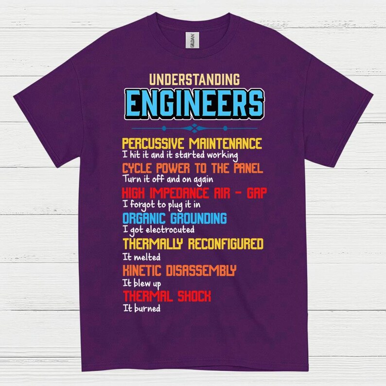 May include: A purple t-shirt featuring the text "UNDERSTANDING ENGINEERS" in blue and white. The shirt displays a list of engineering terms in different colours, such as "PERCUSSIVE MAINTENANCE" and "THERMAL SHOCK".