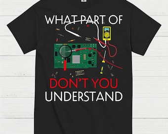 May include: Black t-shirt with the text "WHAT PART OF DON'T YOU UNDERSTAND" in white. The shirt features a graphic of a circuit board, magnifying glass, and a multimeter, suggesting an electronics theme.