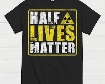 May include: Black t-shirt with a distressed yellow and white graphic. The graphic reads "HALF LIVES MATTER" inside a yellow rectangle with a radiation symbol. The shirt is made of a soft material.