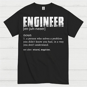 May include: Black t-shirt with the word "ENGINEER" in large, distressed white letters. Below the word is the phonetic pronunciation and a definition of the word "engineer". The definition includes the phrase "wizard, magician."