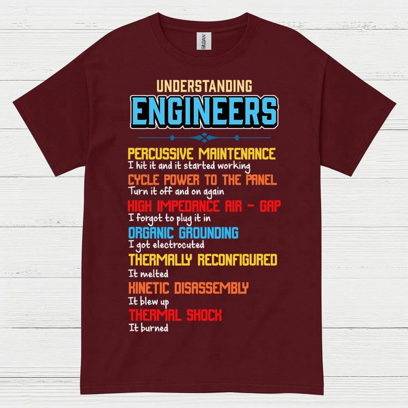 May include: A maroon t-shirt featuring the text "UNDERSTANDING ENGINEERS" in blue and white. The shirt displays a list of humorous engineering phrases in various colours, such as "Percussive Maintenance" and "Thermal Shock."