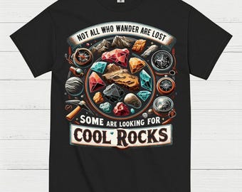 May include: Black t-shirt with a colorful graphic featuring gemstones, compasses, and the text "NOT ALL WHO WANDER ARE LOST SOME ARE LOOKING FOR COOL ROCKS". The design includes a pickaxe and a mountain range.