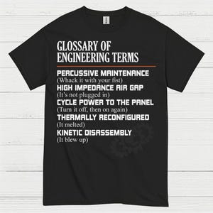 May include: Black t-shirt with white text that reads "GLOSSARY OF ENGINEERING TERMS." The text includes humorous definitions for engineering terms like "Percussive Maintenance" and "Kinetic Disassembly." A gear graphic is in the lower right corner.