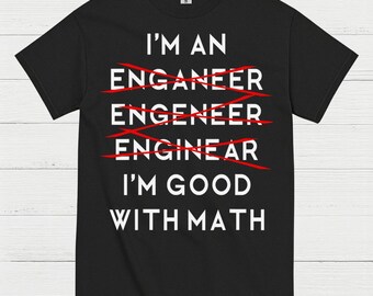 May include: Black t-shirt with white text that reads "I'M AN ENGINEER I'M GOOD WITH MATH." The word "engineer" is crossed out and misspelled multiple times. A humorous design for those in STEM fields.