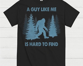 May include: Black t-shirt with a blue graphic of a Bigfoot walking through a forest. The text "A GUY LIKE ME IS HARD TO FIND" is printed above and below the graphic in blue.