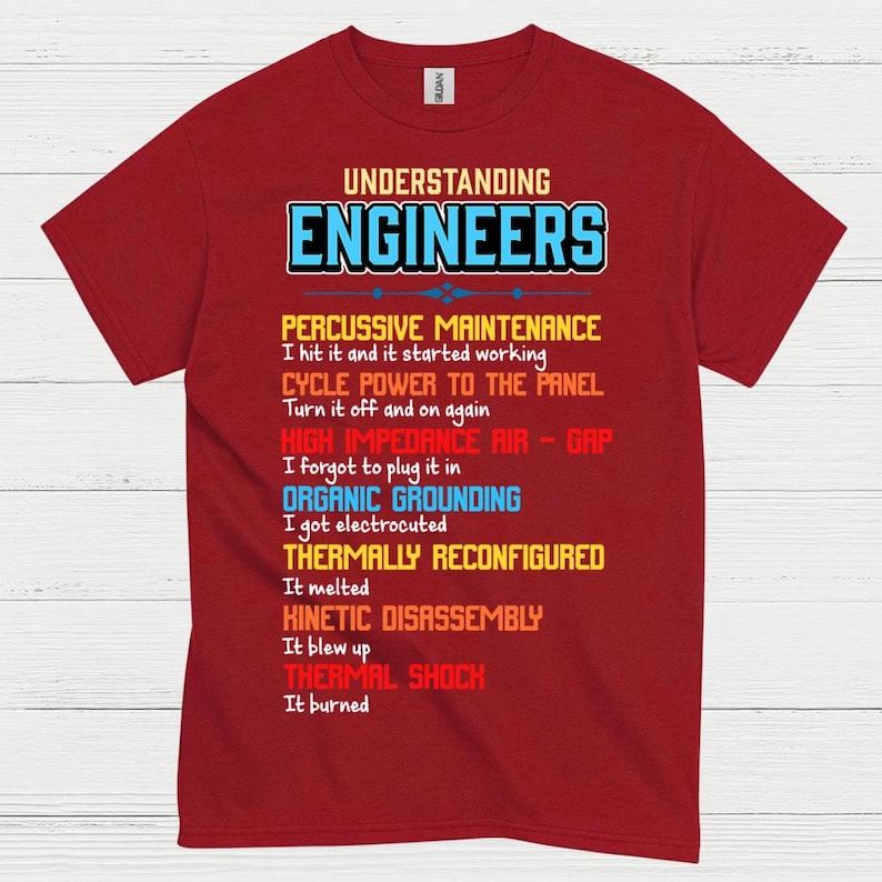 May include: A maroon t-shirt featuring the text "UNDERSTANDING ENGINEERS" in blue and white. The shirt lists humorous engineering troubleshooting methods, such as "Percussive Maintenance" and "Thermal Shock."