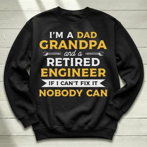 May include: A black long-sleeve crewneck sweatshirt featuring yellow and white text that reads I'M A DAD GRANDPA and a RETIRED ENGINEER IF I CAN'T FIX IT NOBODY CAN, with two small wrench icons flanking the word and.
