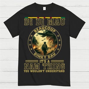 May include: Black t-shirt with a circular graphic featuring a soldier, aircraft, and text. The text includes "DI DI MAU," "BEAUCOUP," "DINKY DAU," and "IT'S A NAM THING YOU WOULDN'T UNDERSTAND." The graphic has a military theme.