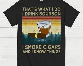 May include: Black t-shirt with a graphic design. The design features a glass of bourbon, a cigar, and text that reads "THAT'S WHAT I DO I DRINK BOURBON I SMOKE CIGARS AND I KNOW THINGS."