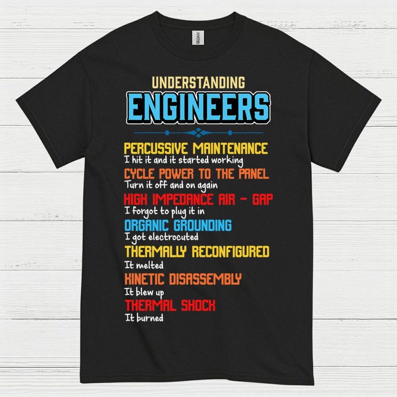 May include: Black t-shirt featuring the text "UNDERSTANDING ENGINEERS" in blue and white. The shirt lists humorous engineering troubleshooting steps in various colours, including "PERCUSSIVE MAINTENANCE" and "THERMAL SHOCK."
