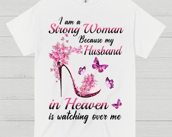 May include: White t-shirt with a graphic design. The design features a high-heeled shoe adorned with pink flowers and butterflies. Text reads "I am a Strong Woman Because my Husband in Heaven is watching over me."