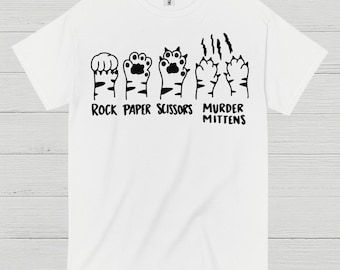 May include: White t-shirt with a black graphic of cat paws representing rock, paper, scissors, and murder mittens. The text "ROCK PAPER SCISSORS MURDER MITTENS" is printed below the paws. The shirt is made of a soft material.