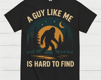May include: Black t-shirt with a Bigfoot graphic. The design features a silhouette of Bigfoot walking in front of a sunset with the text "A Guy Like Me Is Hard To Find" in a white and tan font.