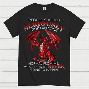 May include: Black t-shirt featuring a red dragon illustration with large wings. The text on the shirt reads "PEOPLE SHOULD SERIOUSLY STOP EXPECTING NORMAL FROM ME... WE ALL KNOW IT'S NEVER GOING TO HAPPEN!"