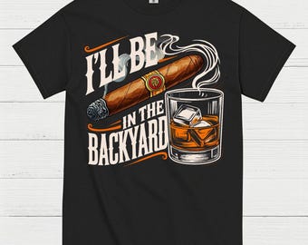 May include: Black t-shirt with a graphic design featuring a lit cigar, a glass of whiskey with ice cubes, and the text "I'll Be In The Backyard" in white and orange. The design has a vintage, masculine aesthetic.