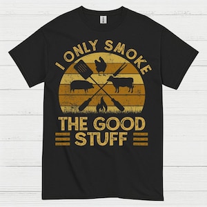 May include: Black t-shirt with a graphic design featuring a sunset, crossed grilling tools, and silhouettes of a pig, chicken, and cow. The text reads "I ONLY SMOKE THE GOOD STUFF."