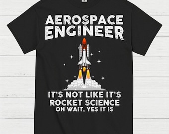 May include: Black t-shirt with white text that reads "AEROSPACE ENGINEER." Below the text is a graphic of a space shuttle launching, with flames and smoke. The text "IT'S NOT LIKE IT'S ROCKET SCIENCE OH WAIT, YES IT IS" is below the graphic.