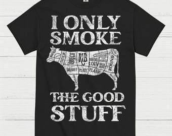 May include: Black t-shirt with white text and a diagram of a cow's cuts of meat. The text reads "I ONLY SMOKE THE GOOD STUFF". The cow diagram labels various cuts like "RIB", "SHORT LOIN", and "FLANK".