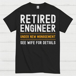 May include: Black t-shirt with white text that reads "RETIRED ENGINEER UNDER NEW MANAGEMENT SEE WIFE FOR DETAILS". The text is in a bold, sans-serif font. The shirt is a crew neck style.