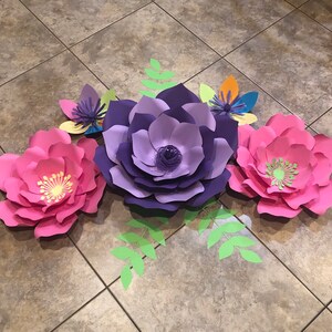May include: Three large paper flowers in pink, purple, and light purple with green leaves. The flowers are layered and have a 3D effect.