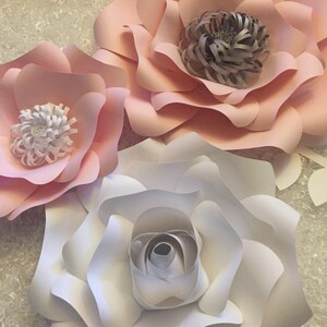 May include: Three paper flowers, one white and two pink, with layered petals and a center made of curled paper. The flowers are arranged on a white background.