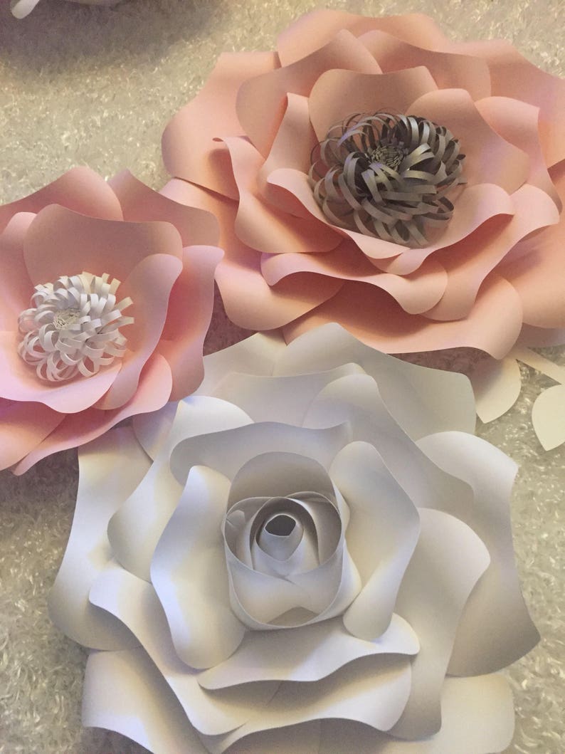 May include: Three paper flowers, one white and two pink, with layered petals and a center made of curled paper. The flowers are arranged on a white background.
