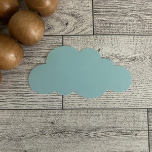 May include: A light blue cloud-shaped cutout sits on a wooden surface, with several wooden spheres in the upper left corner. The cloud is a soft, pastel color, and the wood has a gray and white grain pattern.