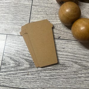 May include: A stack of brown paper coffee cup cutouts. The cutouts are stacked on top of each other and have a rounded top and a straight bottom.