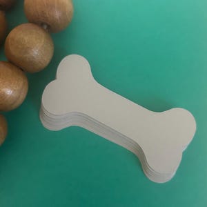 May include: A stack of beige dog bone shaped paper tags. The tags are on a teal background.