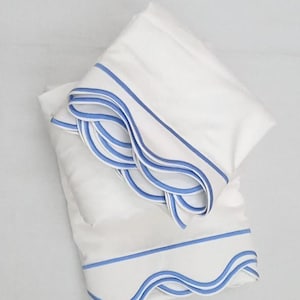 May include: Two white pillowcases with light blue scalloped edges and trim. The pillowcases are stacked on top of each other, showcasing the detailed design. The bedding has a clean, elegant aesthetic.