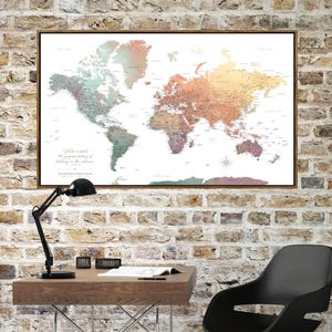 May include: A framed world map with a brown wooden frame, displayed on a brick wall. The map features a colour palette of greens, oranges, and browns. The text on the map reads, "Find a world, the gorgeous feeling of belonging in the universe."