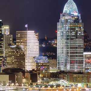 May include: A night view of a city skyline with several tall buildings, including a skyscraper with a pointed roof. The buildings are illuminated with lights, creating a bright and vibrant scene.
