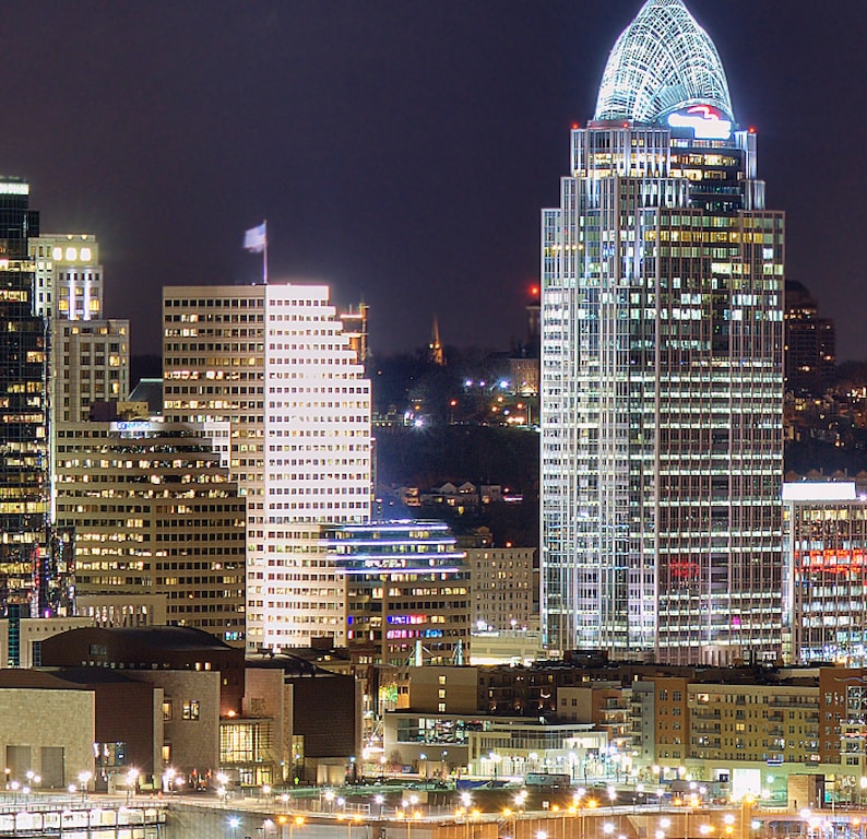 May include: A night view of a city skyline with several tall buildings, including a skyscraper with a pointed roof. The buildings are illuminated with lights, creating a bright and vibrant scene.
