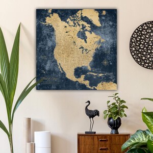 May include: A square wall art piece featuring a detailed map of North America in gold against a dark blue, textured background. The map includes geographical details and a compass rose. The text "Paul & Janice" is at the bottom.